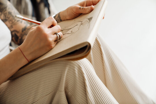 Close up of woman's hands drawing in sketchbook while sitting on floor