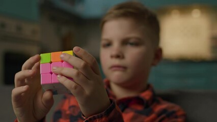 Kid Playing with Cube Puzzle Close Up. Smart kid plays with cube jigsaw sitting on couch at home.