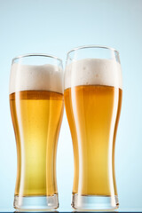 Fizzy yellow beer poured to tall glasses on light blue.