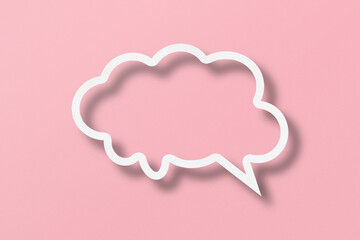 White paper cut out speech bubble shape set on pink paper background.