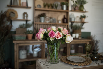 Bouquet of roses on a wooden table. In the background is a boho or rustic kitchen interior. The concept of home comfort. The concept of International Women's Day March 8, holiday, spring.