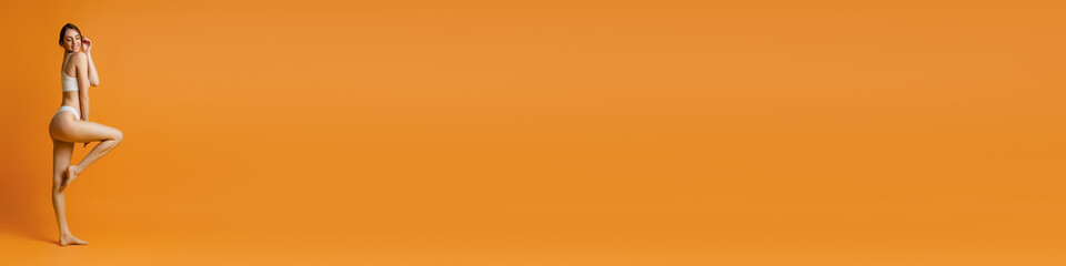 Young beautiful girl posing in cotton underwear over orange studio background. Concept of beauty, body and skin care, fitness, health, spa, cosmetics, ad