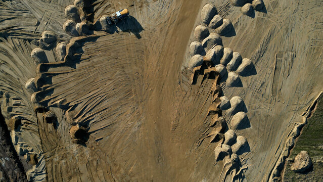 Arial view of open pit sand mine. A front loader loads sand from piles. Heavy mining machinery working in a quarry. lots of wheel tracks and piles of sand like desert dunes or breasts, dry, sandy,sell