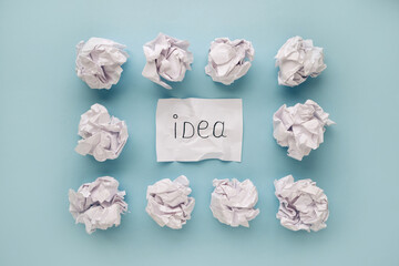 sheet of paper with word idea and crumpled paper balls on blue background. Brain storming concept