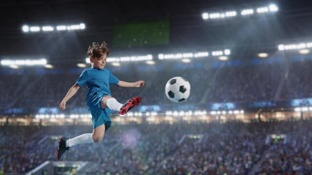 Aesthetic Shot Of Athletic Child Soccer Football Player Jumping And Kicking Ball Mid-Air On Stadium WIth Crowd Cheering. Super Slow Motion Captures A Boy Scoring a Goal on Junior World Championship.