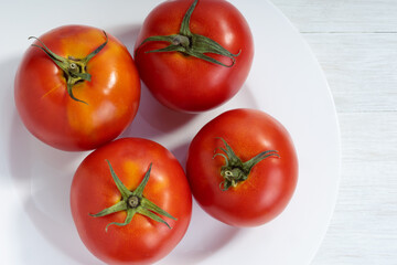 Red whole tomatoes on a white plate. Place for text. Top view.