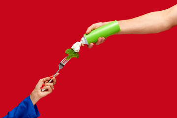 Food pop art photography. Female hand holding broccoli on fork with whipped cream against red studio background. Healthy eating. Concept of art and creativity. Complementary colors. Copy space for ad