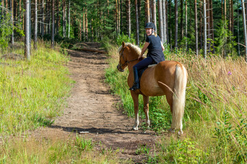 Woman horseback riding in forest trail