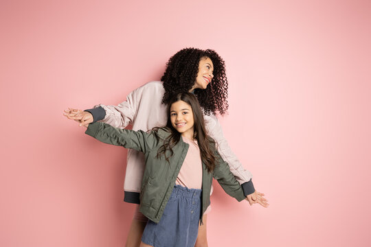 Smiling woman holding hands of preteen kid on pink background.