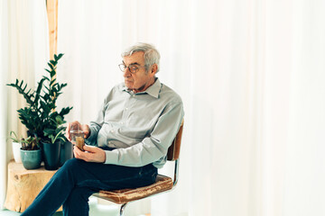 senior person sitting and holding glass of water is taking pills