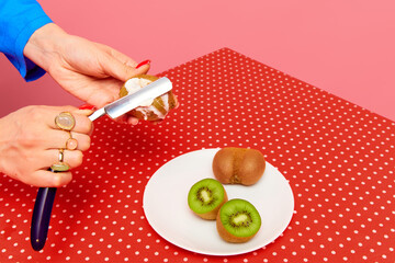 Female hand putting sause on kiwi with razor against pink studio background. Food pop art photography. Creativity and art. Complementary colors. Copy space for ad, text
