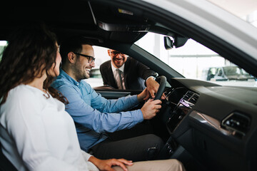 Middle age couple choosing and buying car at car showroom. Car salesman helps them to make right decision.