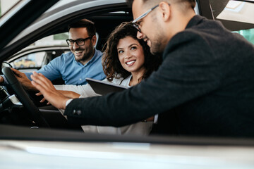 Middle age couple choosing and buying car at car showroom. Car salesman helps them to make right decision.