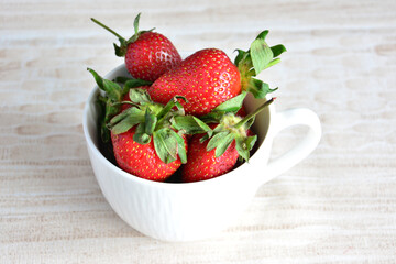 A white cup of fresh garden strawberries isolated on beige background, macro 