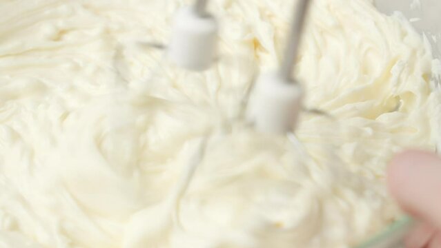Close up shot of whipping heavy cream in glass bowl using hand mixer until stiff peaks form; homemade dessert