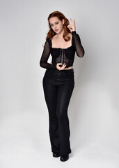Full length portrait of beautiful woman with long red hair wearing black corset top and leather...