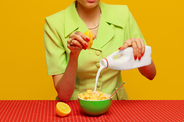 Cropped image of woman in retro suit putting milk and squeezing lemon juice into cereal against pink studio background. Food pop art photography. Complementary colors. Copy space for ad, text