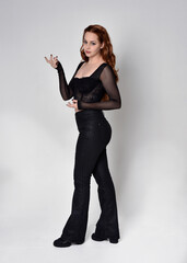 Full length portrait of beautiful woman with long red hair wearing black corset top and leather...