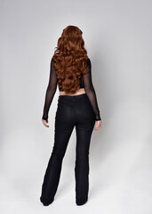 Full length portrait of beautiful woman with long red hair wearing black corset top and leather...