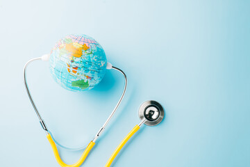 World Health Day. Top view yellow doctor stethoscope wrapped around world globe isolated on pastel...