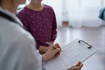 Doctor woman and kid patient at home. The pediatrician fills up medical form, close up. Medicine, healthcare concepts