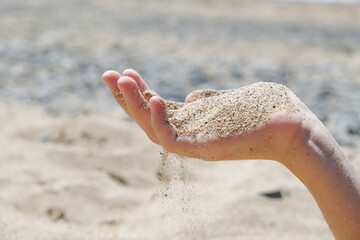 A young woman's hands hold sand on the beach. A natural summer background.