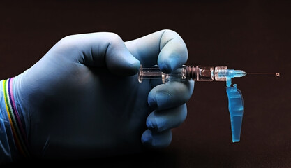 Hand with blue glove and bracelet of the LGBT collective with a vaccine, on black background