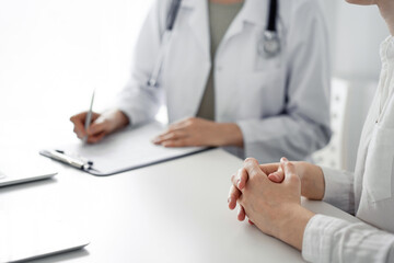 Doctor and patient discussing current health examination while sitting at the desk in clinic office. The focus is on female patient's hands, close up. Perfect medical service and medicine concept.