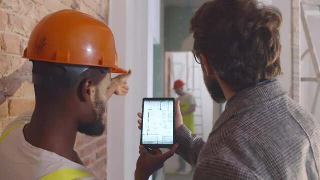 Home owner and builder discuss house blueprint on digital tablet. Realtime