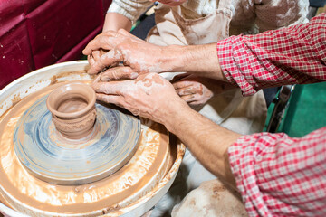 master class on modeling clay, creating a vase, bowl, pot on potter's wheels in the workshop. the master helps the child to create.