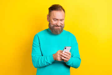 Photo of cheerful attractive man wear stylish clothes use iphone samsung texting sms share repost isolated on yellow color background