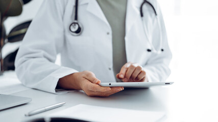 Unknown doctor woman sitting and writing notes at the desk in clinic or hospital office, close up.  Medicine concept.