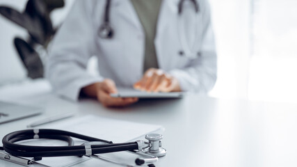Stethoscope lying at doctor's working desk, close up. Physician uses tablet computer at the background. Medicine concept.