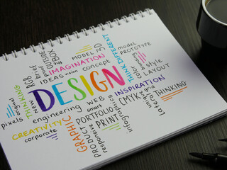 Colorful DESIGN word cloud handwritten in notebook with espresso and pens on black wooden desk