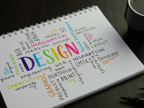 Colorful DESIGN word cloud handwritten in notebook with espresso and pens on black wooden desk