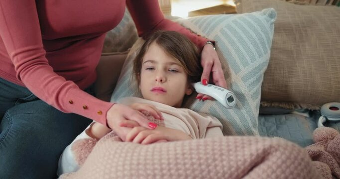Mother parent checking temperature of her sick daughter with digital ear thermometer