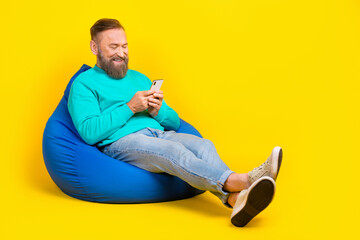 Full body photo of attractive grandpa sit beanbag relax chatting device wear trendy aquamarine...