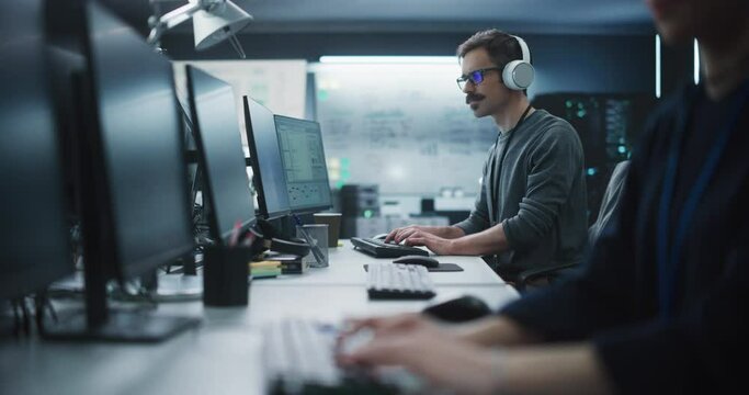 System Administrator Working in a Research E-Business Facility on a Desktop Computer. Focused Software Developer in Casual Clothes Wearing Headphones and Updating Server System Database