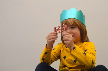 A little boy in a crown plays with a raashan. Jewish holiday Purim. Birthday, happy holidays. Isolate on white background, space for text