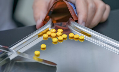 Selective focus on yellow tablets pills on stainless tray with blur hand of pharmacist or pharmacy...