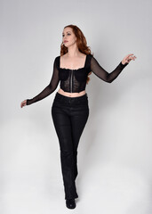 Full length portrait of beautiful woman with long red hair wearing black corset top and leather...