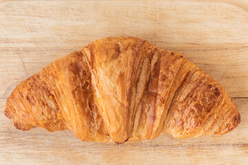 Flat lay of soft croissant with golden crust on a wooden cutting board, top close-up view. Beige background. Traditional French pastry