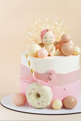 Birthday cake for a girl with pink pastel cream cheese frosting decorated with unicorn figure, chocolate spheres and caramel candies on the beige background.