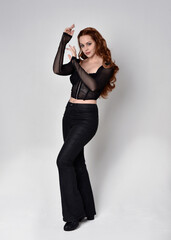 Full length portrait of beautiful woman with long red hair wearing black corset top and leather...