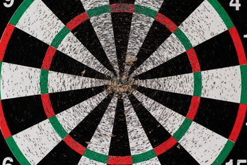 Old dartboard punctured by darts on light wall. Background of an old shabby round target in holes...