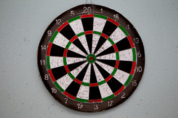 Old dartboard punctured by darts on light wall. Background of an old shabby round target in holes...