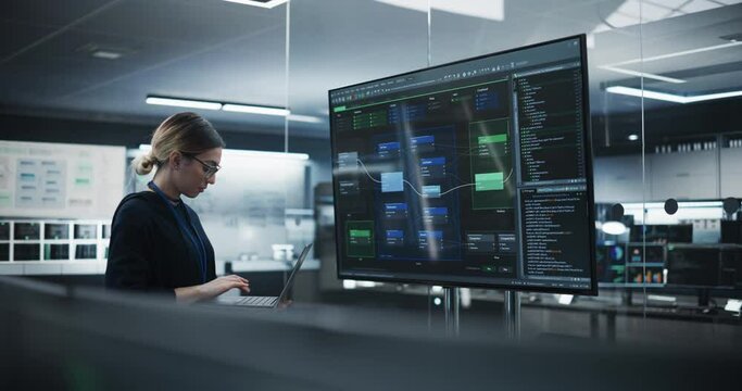 Beautiful Multiethnic Lead Software Engineer Standing Alone in a Meeting Room, Using a Big TV Display to Review a Computer Program Created by Research and Development Department