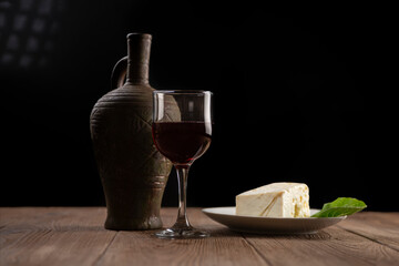 jug with wine, homemade cheese and a glass on a wooden table