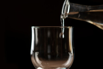 girl hands pouring red wine into a glass from a clay bottle on a black background