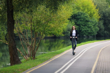 A young woman in stylish clothes rides an electric scooter on a bike path